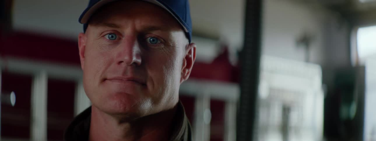 Firefighter with a blue cap and a coat looking sideways turns his gaze to the camera in a fire station
