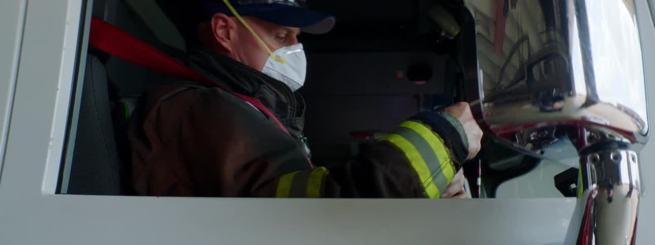 A firefighter with a flashlight in a fire truck wearing a hat and a mask