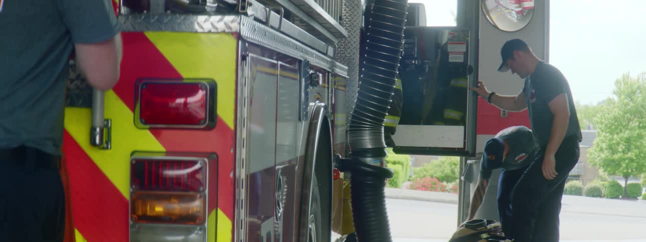 A group of firefighters remove their personal protective equipment and place it inside a fire engine