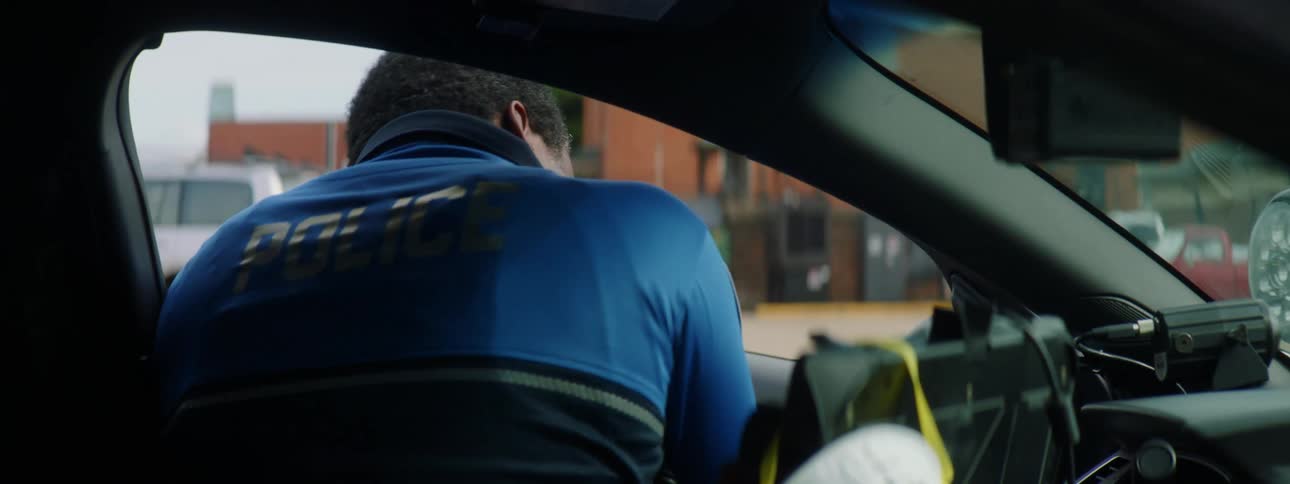 Policeman gets into his vehicle as a mask hangs from the monitor inside