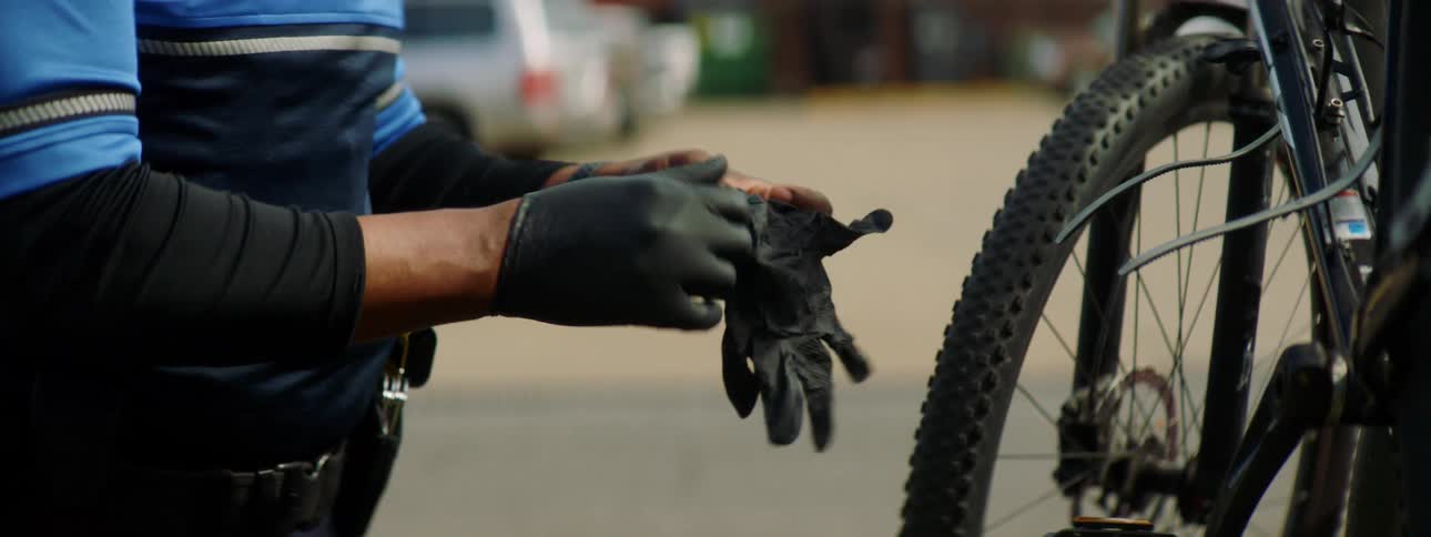 An officer is putting on his gloves by the bicycle