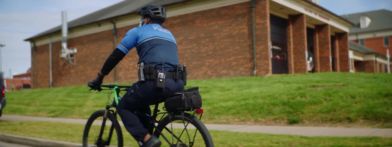 Police officer with a black helmet and a face mask rides a bicycle on a road
