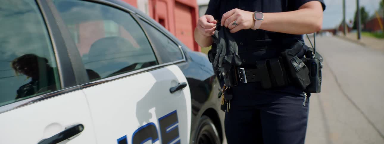 Female police officer takes black latex gloves from utility belt before boarding patrol car