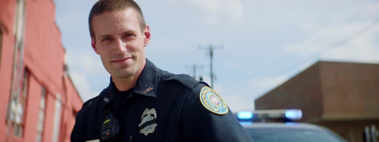 Police officer with a police uniform and standing by a police car raises his head and looks at the camera in the street
