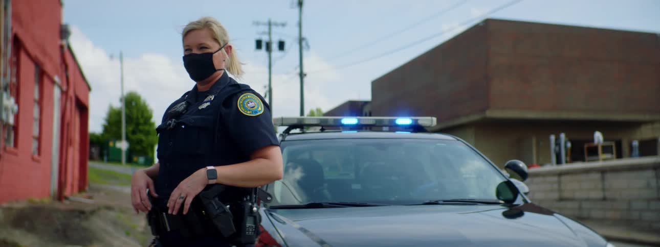 A female police officer stands outside of her vehicle wearing a medical mask