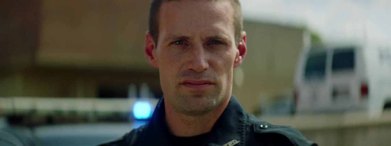 Male police officer standing in front of patrol car parked on the street of a small town