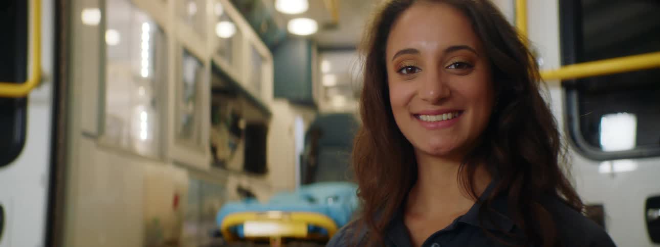 A woman staring and smiling with an ambulance and a stretcher in the background