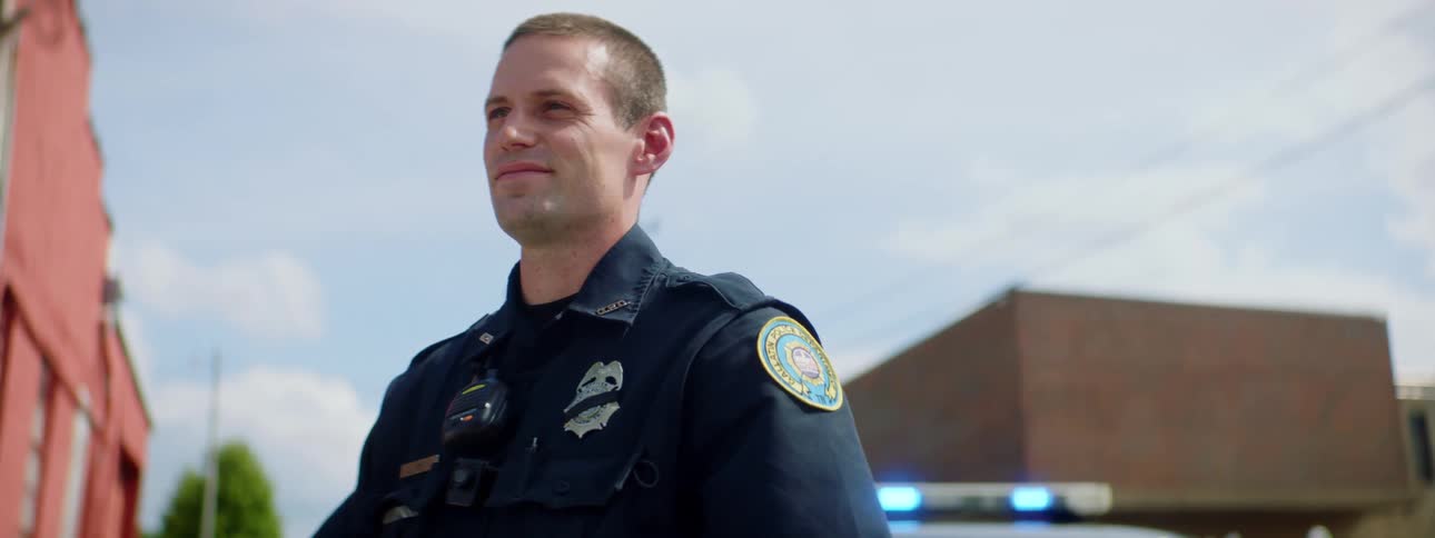Police officer stands in front of patrol car in the street of a small town at day