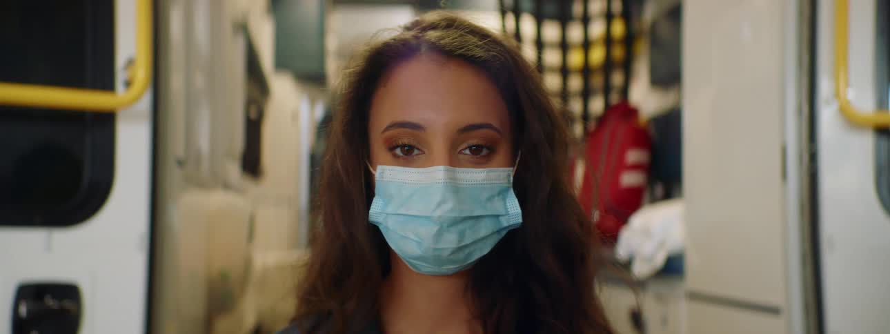 Female paramedic wearing face mask smiles in front of an ambulance