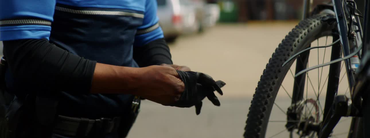 Police officer puts on black latex gloves in front of a bicycle on a street