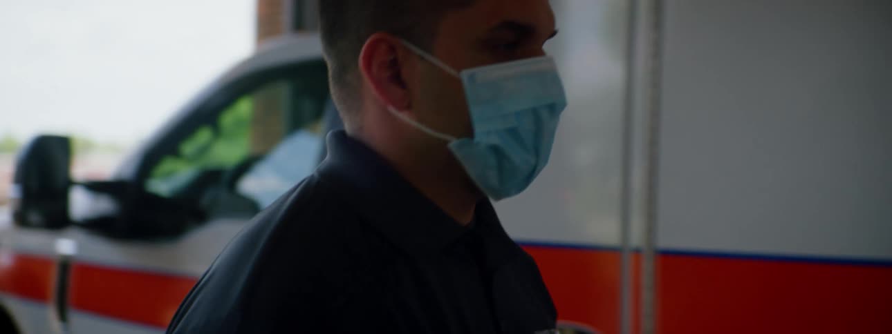 Paramedic puts a face mask while walking towards an ambulance parked inside a fire station