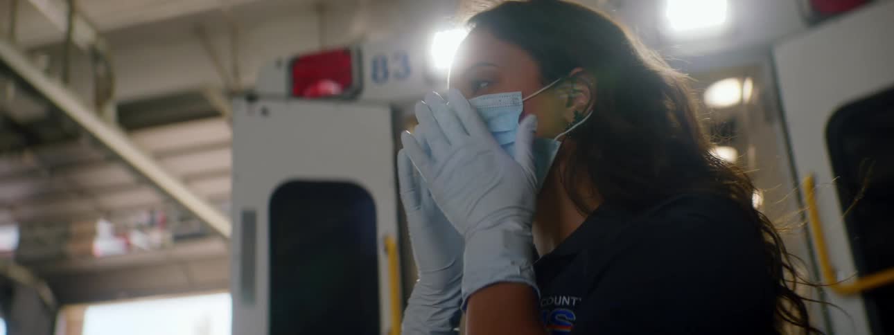 Paramedic wearing gloves puts a face mask on in front of an ambulance