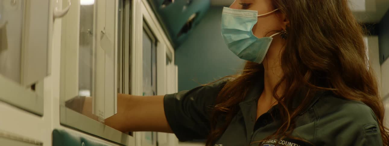 Woman wearing a medical mask and gloves retrieves medical supplies from a cabinet