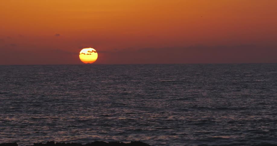 The sun is almost set behind the ocean
