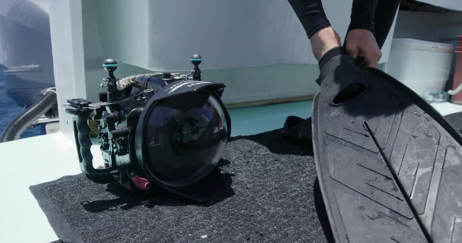 A diver puts on his flippers by a camera