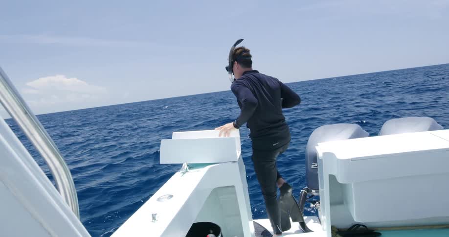 A man adjusts the snorkel on his face and walks off the edge of a boat into the ocean