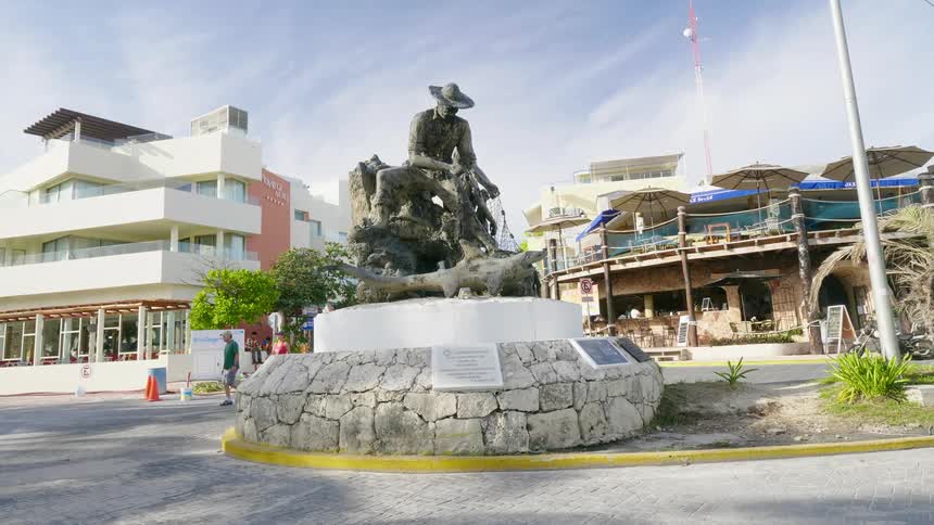 Statue of a fisherman capturing a shark with a net on the street near a restaurant
