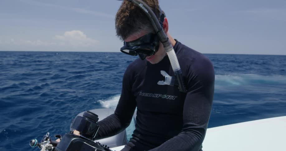 Scuba diver wearing neoprene suit and snorkel checks an underwater camera while sitting in a yatch