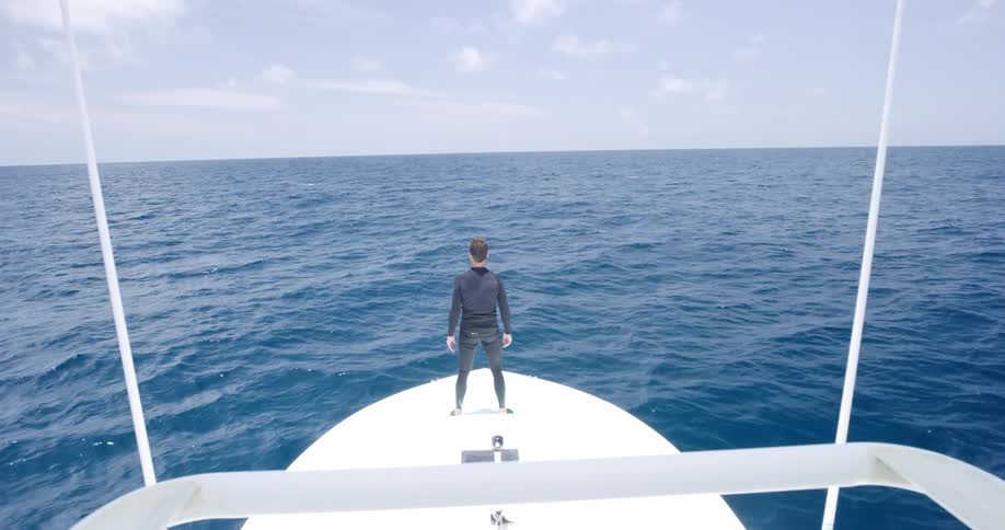 A man is standing on a ship as its moving through the ocean