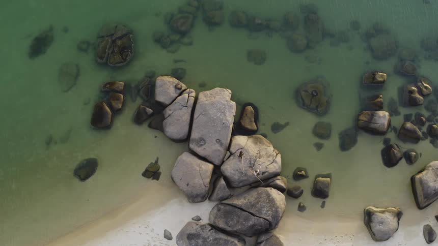 Birds eye view of people walking across large rocks on the shore