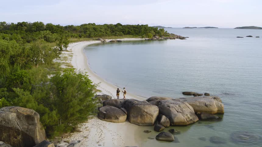 Two men climb over the rocks to walk on the beach near the ocean
