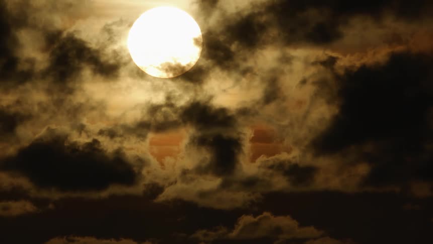 Bright yellow full moon in the sky behind dark clouds