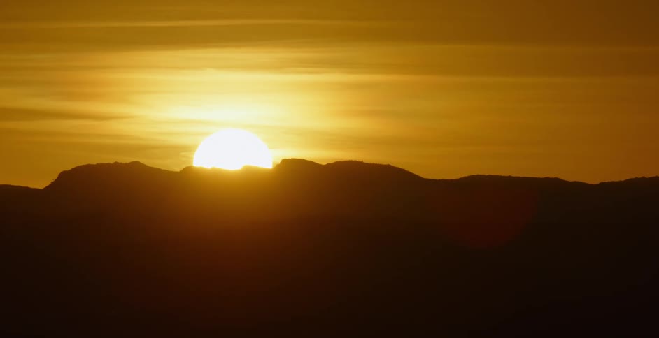 The sun slowly rises from behind a mountain ridge