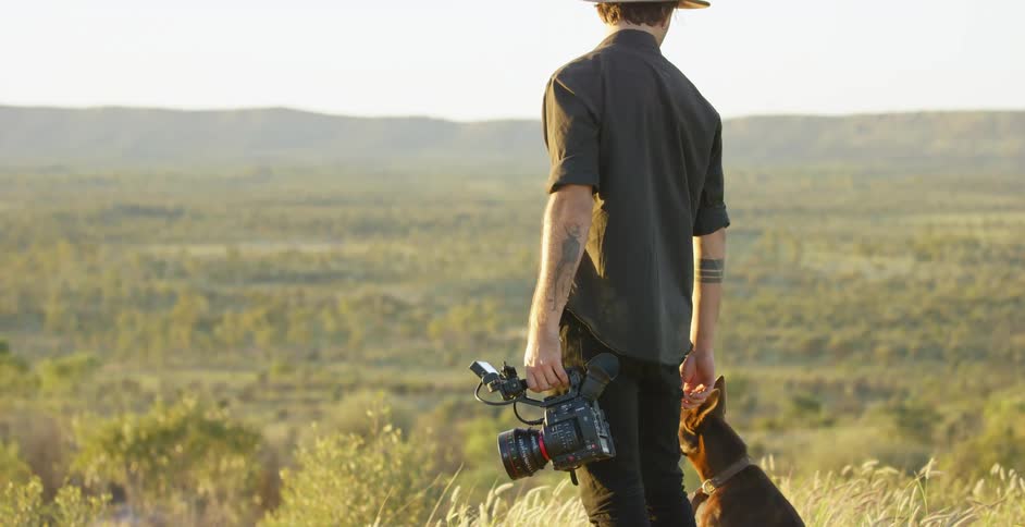 A photographer stands in a field with his dog