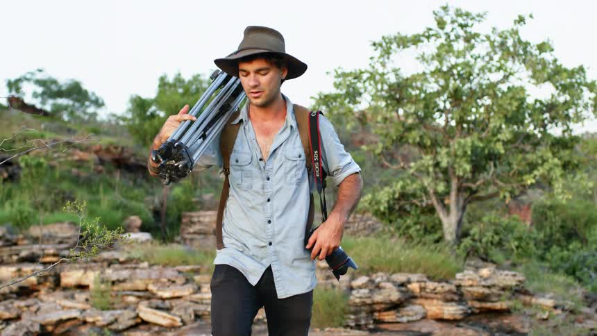 Photographer climbs the rocks on the hills with a tripod on his shoulder
