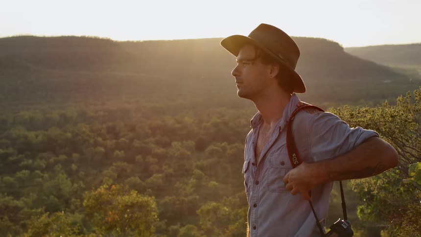 Man with a camera stands atop of a hill in the desert wilderness at sunset