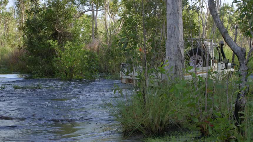 A person off roading drives their truck through a river