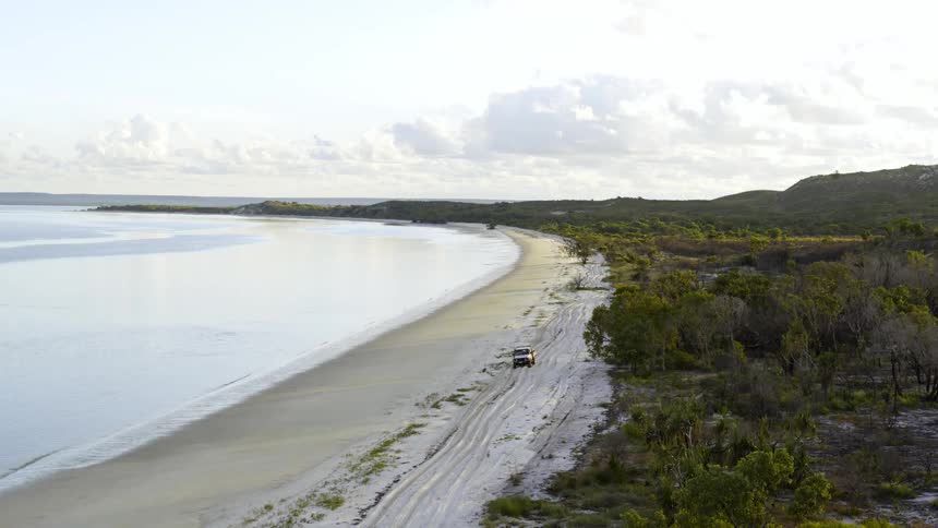 All terrain vehicle drives in the sand near the shoreline of a tropical beach at morning