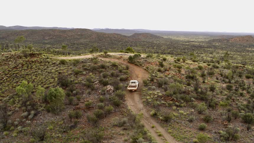 A truck drives up a shrub covered hill in the wilderness