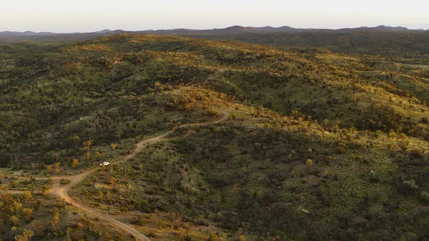 Car driving on a dirt road through the hills covered in shrubs and bushes at sunset