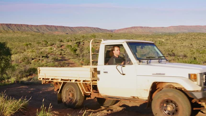 A man drives his truck over a rough dirt road with his dog