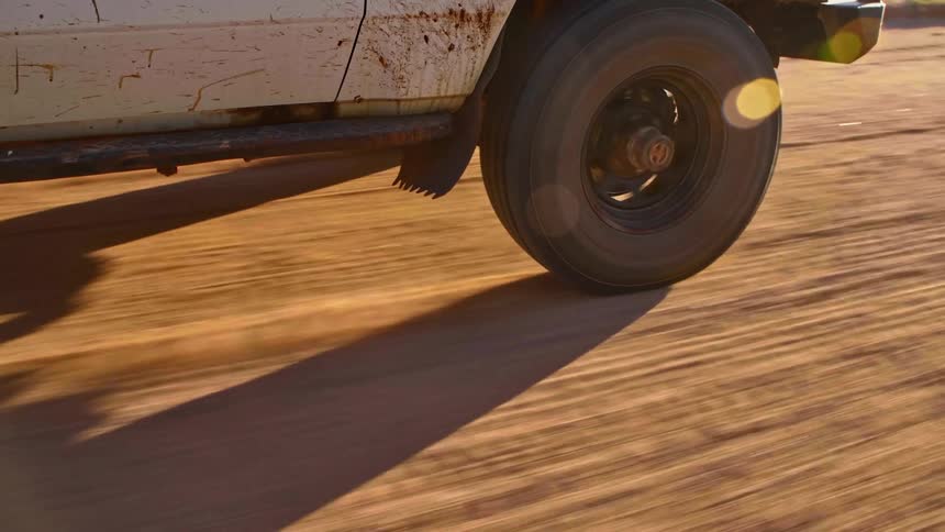 A car drives on a dirt road on a sunny day