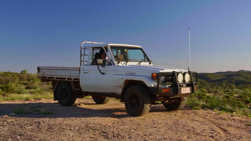 A man parks his truck in a vast hilly countryside before he and his dog exit the vehicle