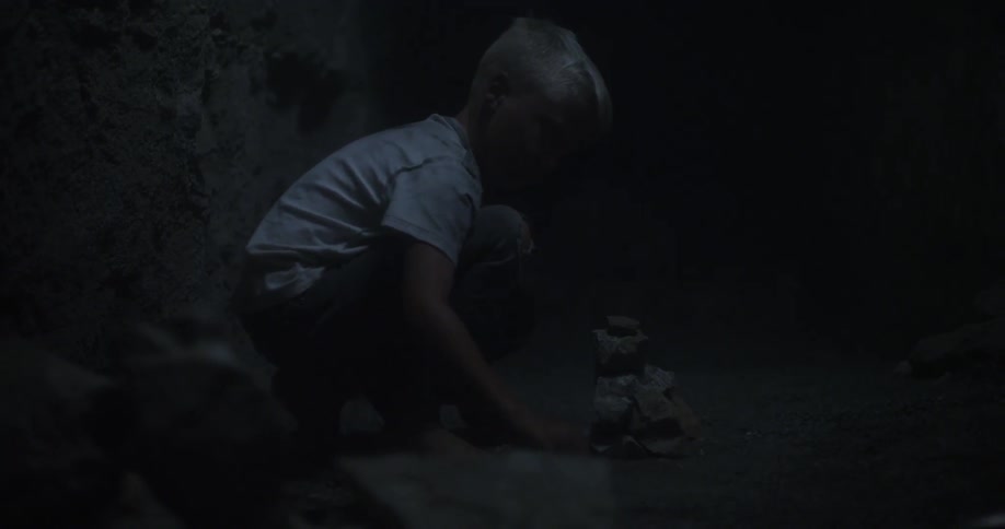 A child is stacking some rocks in a dark cave