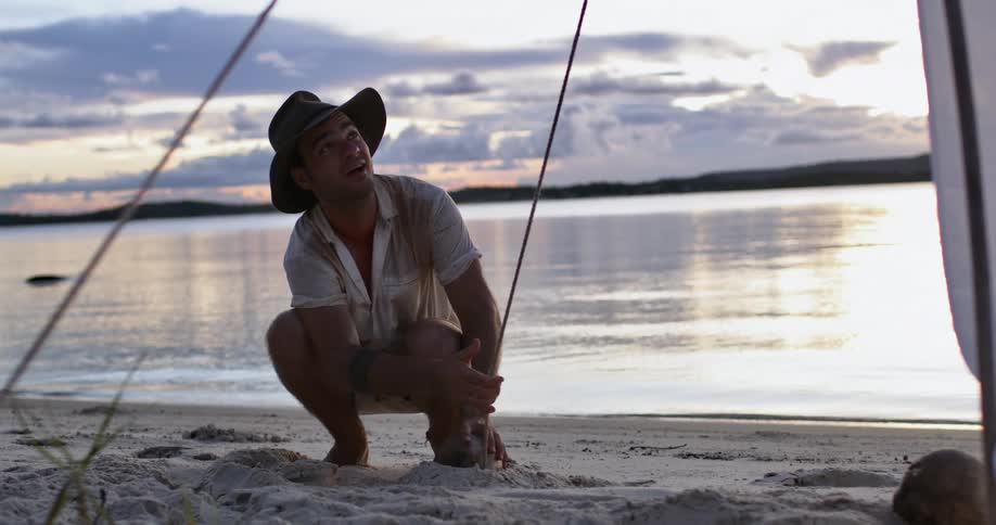 A man flicks the rope of a beach tent while securing it in the sand