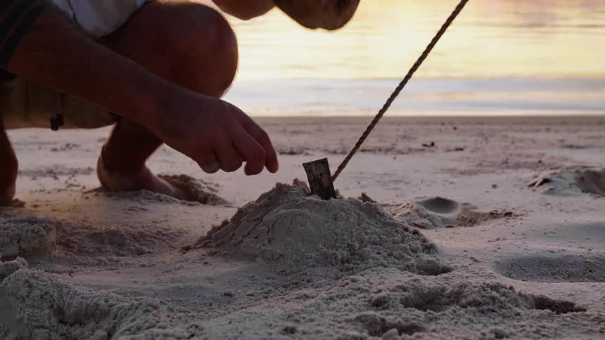 A man on a beach bangs a coconut on a stick