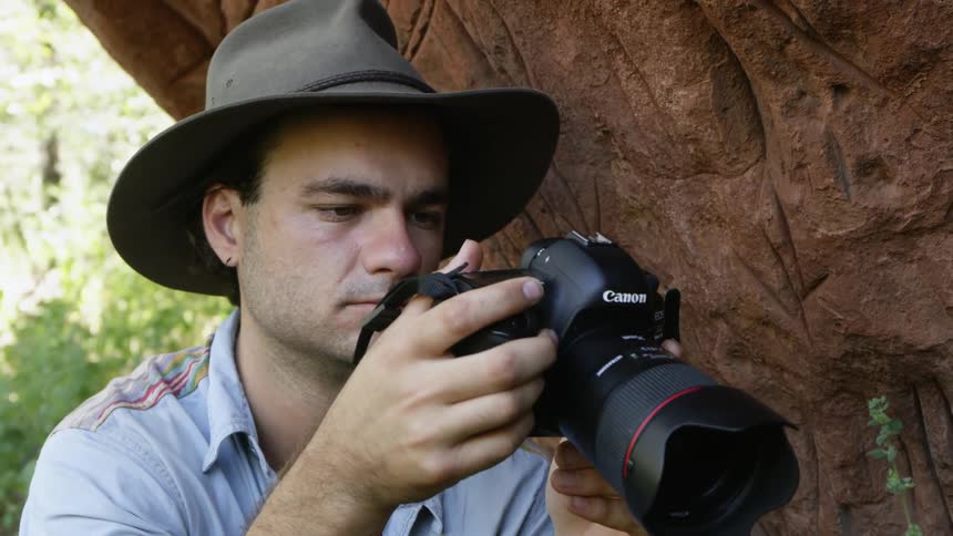 Photographer takes picture standing under overhanging rock wall