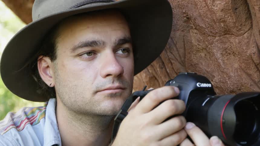 Photographer wearing a hat points a camera and takes pictures outdoors