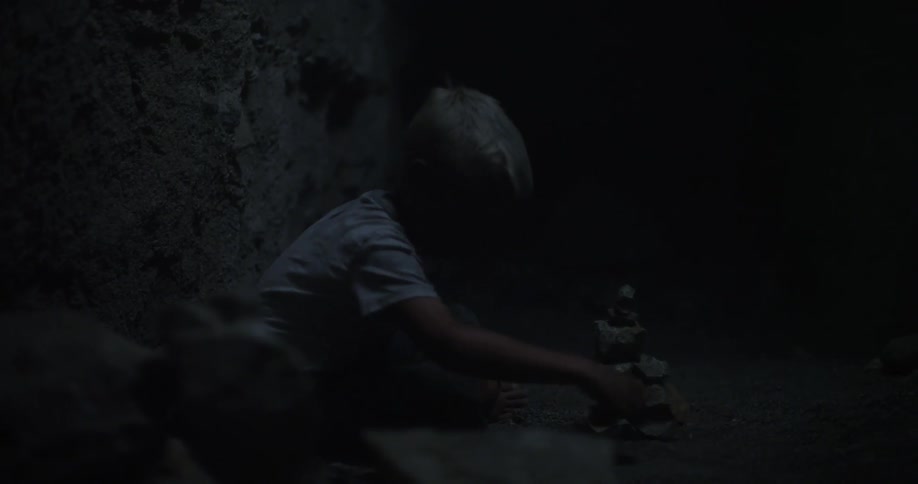 A boy stacks rocks in a dark cave