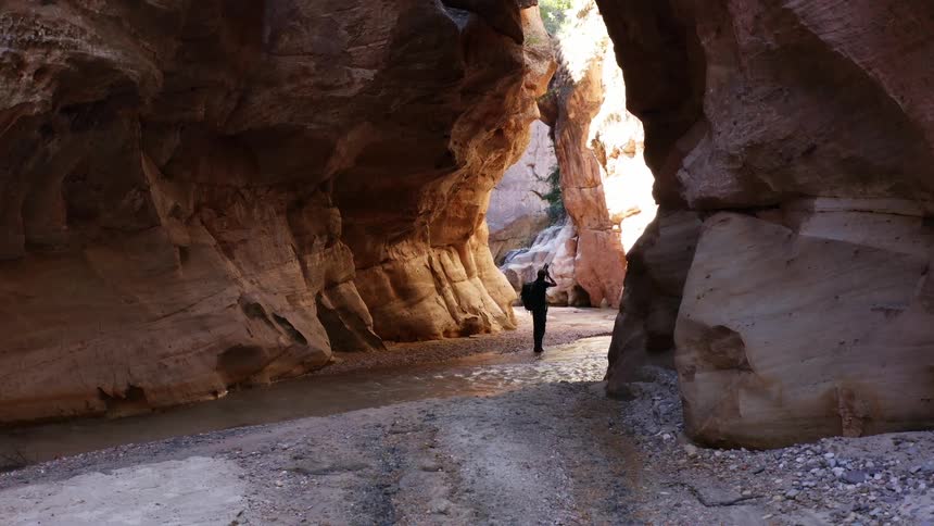 Man walks through a stream in a canyon and takes a photo with a camera