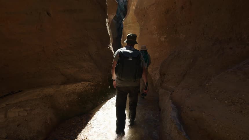 Two people walk through a river and between canyons