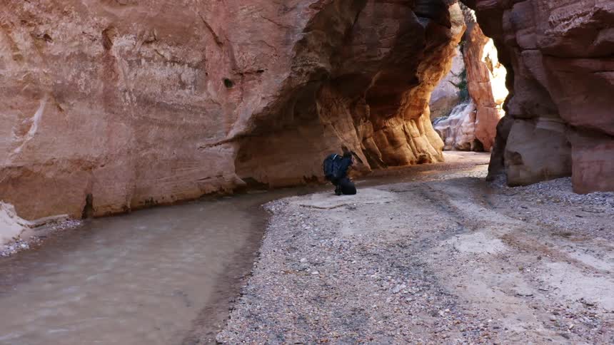 A man walks next to a river and then bends down to take a picture
