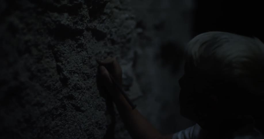 A child writes on a rock wall with a stick