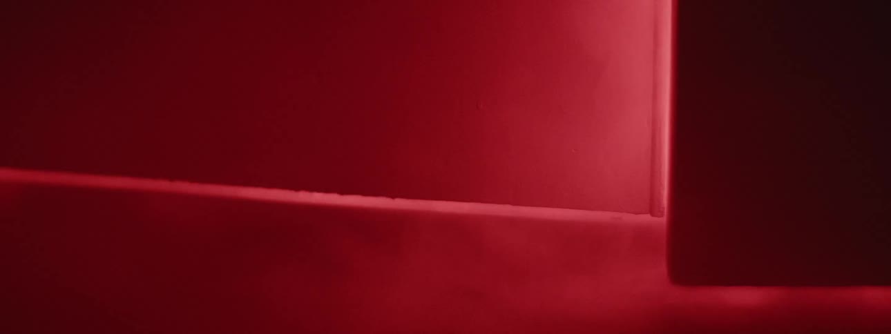 Smoke comes out of a room illuminated with red light as a door slowly opens
