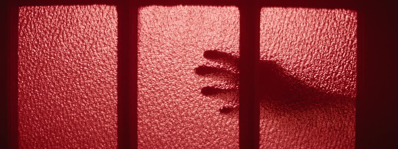 A persons hand on a glass door with red light
