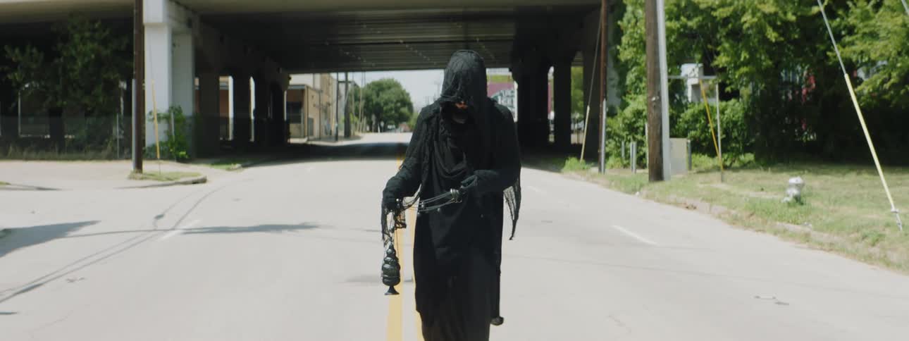 A man with black robes walking down the road swinging a chain censer with smoke